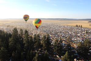 Two hot air balloons hovering over festival near camping area with trees nearby