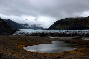 Glacier with clouds, mountains and small pond in front of them